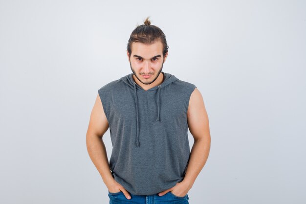 Young fit male in sleeveless hoodie  keeping hands in pockets and looking confident , front view.