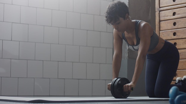 Young fit and tone up mixed race woman doing fitness workout with abs wheel at loft during sunny day