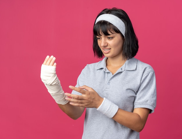 Young fitness girl wearing headband touching her bandaged hand looking unwell feeling pain 