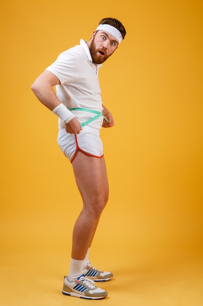 Young fitness man measurig his waist and looking at camera