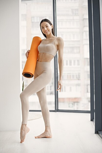 Young fitness woman ready for workout holding orange yoga mat