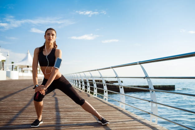 Young fitness woman who makes sport exercises with sea coast behind