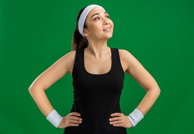 Free photo young fitness woman with headband and armbands looking aside smiling confident with arms at hip