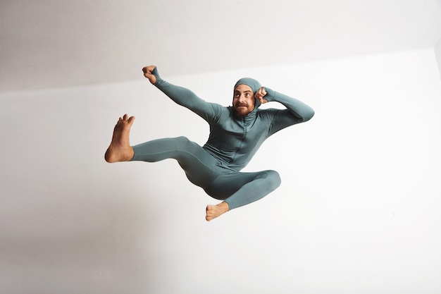 Free Photo young and fitted bearded athlete male wearing his winter snowboardint baselayer thermal suite and having fun acting like a ninja, jumping with leg kicks in air