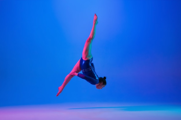 Young flexible girl isolated on blue studio background Young female model practicing artistic gymnastics Exercises for flexibility balance