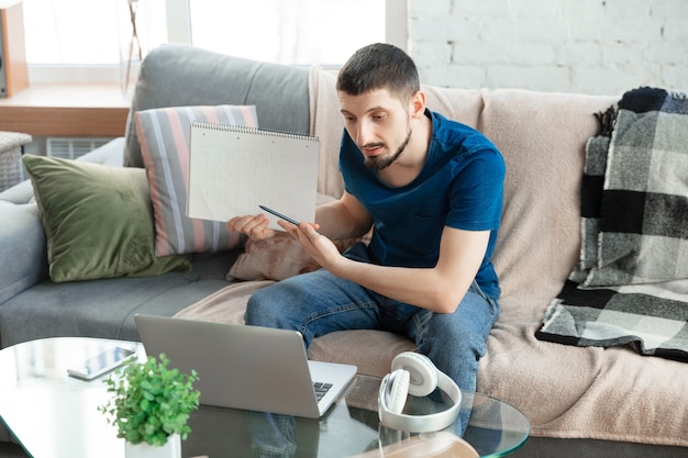 Free photo young focused man studying at home during online courses or free information by hisself