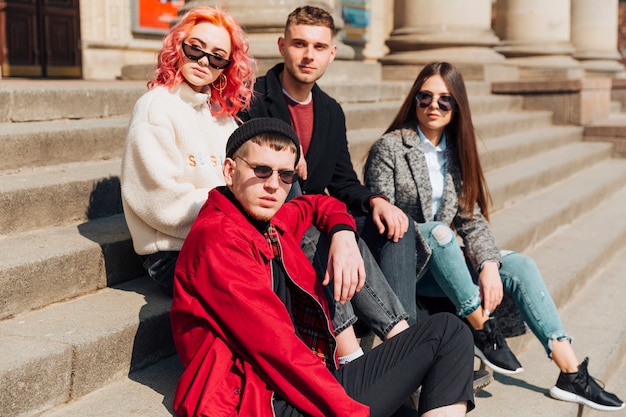 Young friends sitting on stone stairs on city street 