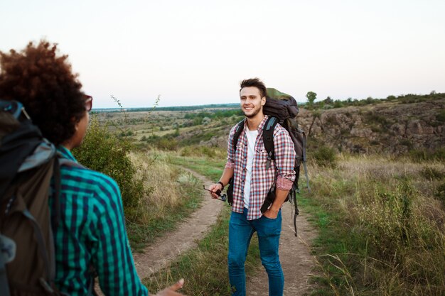 Young friends with backpacks and huskies smiling, traveling in canyon