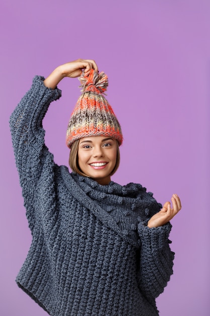 Free Photo young funny beautiful fair-haired woman in knited hat and sweater smiling posing on violet. copy space.