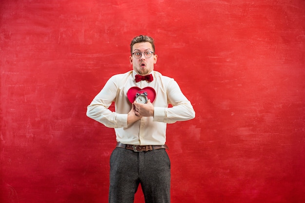 Free Photo the young funny man with abstract heart and clock on red studio. concept - time to congratulate