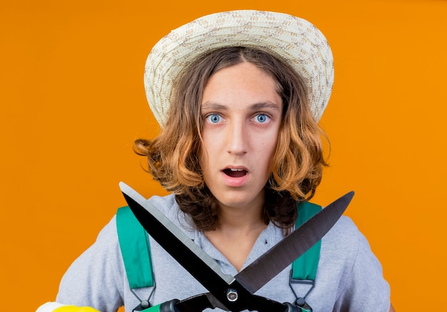 Free Photo young gardener man in rubber gloves wearing jumpsuit and hat holding hedge clippers