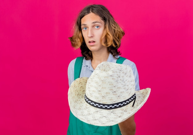 Free photo young gardener man wearing jumpsuit showing his hat being confused