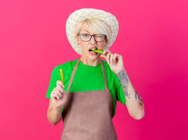 Young gardener woman with short hair in apron and hat holding halves of green chili pepper