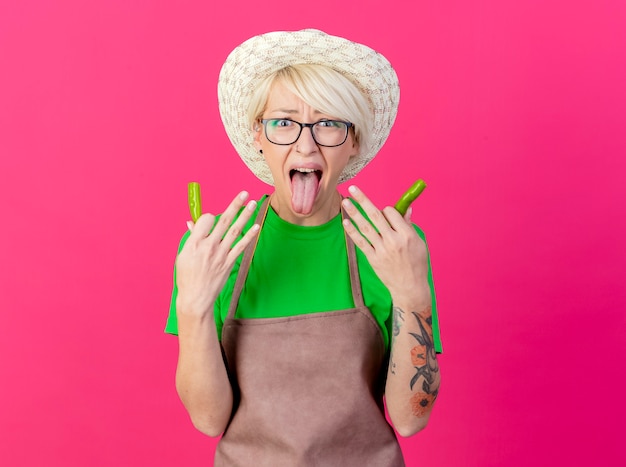 Young gardener woman with short hair in apron and hat holding halves of green chili pepper