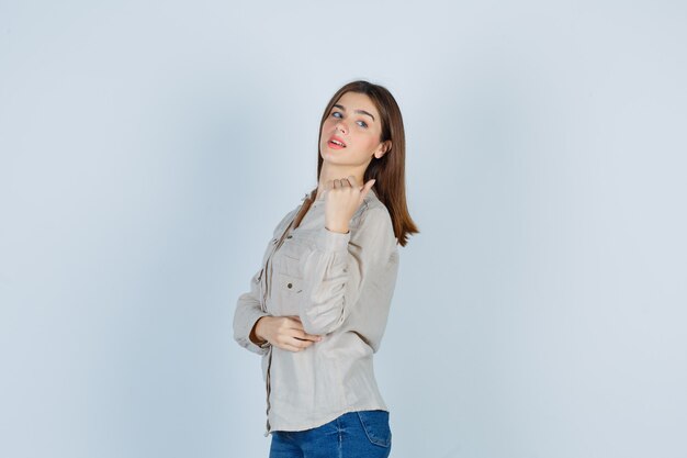 Young girl in beige shirt, jeans clenching fist, looking over shoulder and looking cute , front view.