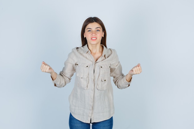 Young girl in beige shirt, jeans clenching fists and looking agitated , front view.