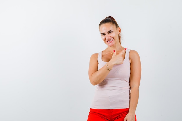 Young girl in beige top and red pants pointing right with index finger and looking happy