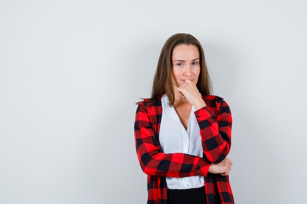 Young girl in checkered shirt, blouse with hand on mouth and looking sensible , front view.