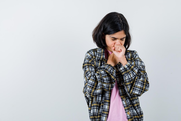 Young girl coughing in checked shirt and pink t-shirt and looking exhausted. front view.