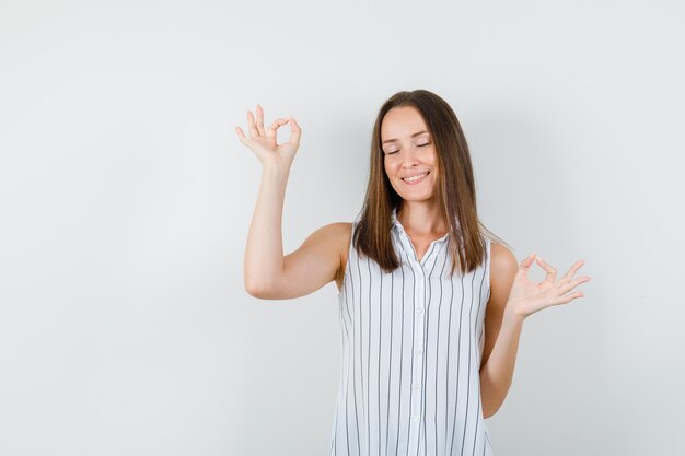 Young girl doing ok sign with closed eyes in t-shirt and looking peaceful. front view.