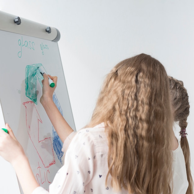 Young girl drawing recycle sign on whiteboard