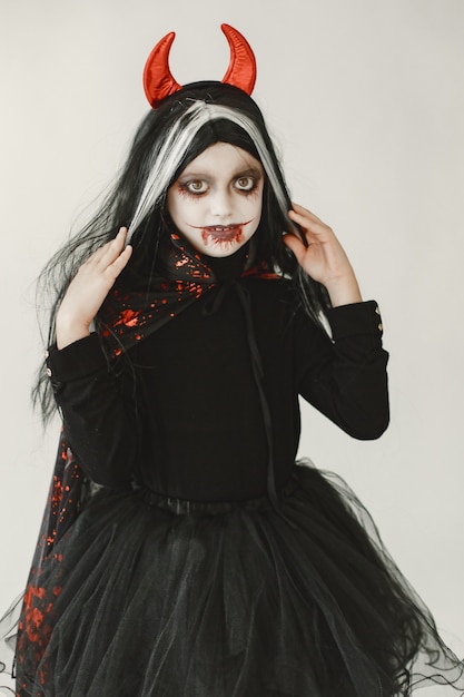 Young girl dressed in black dress as a devil has a two red horns on her head