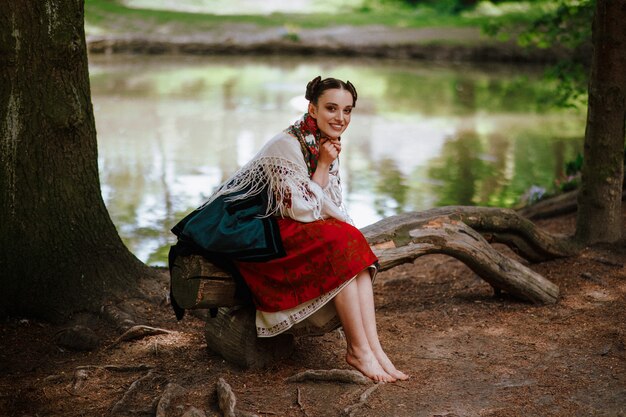 Young girl in a ethnic embroidered dress sitting on a bench near the lake