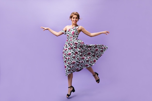 Young girl in fluffy dress jumps on purple background. Lovely beautiful woman in colorful trendy clothes smiling on isolated backdrop.