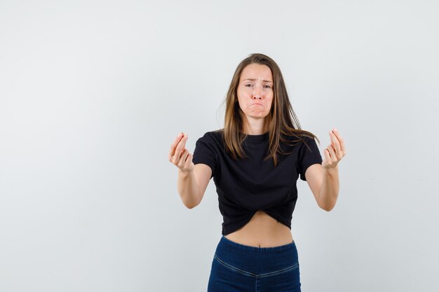 Young girl gesturing with fingers in black blouse, pants and looking mournful.