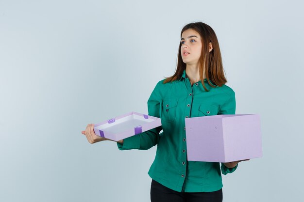 Free Photo young girl in green blouse, black pants opening gift box, looking away and looking focused , front view.