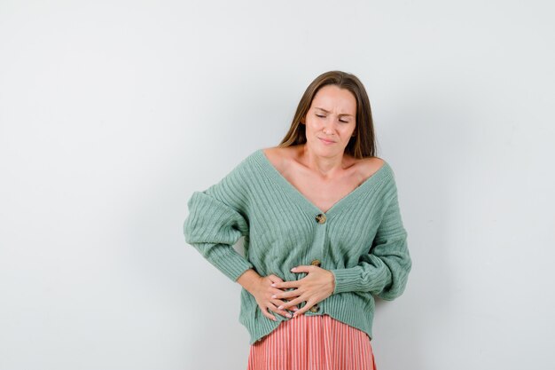 Young girl having bellyache in knitwear, skirt and looking exhausted , front view.