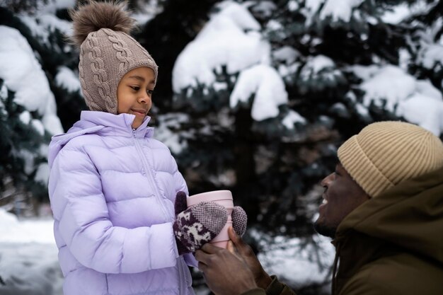 Young girl holding cup of warm drink while out on a winter day with her father