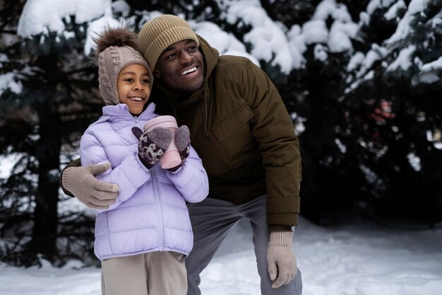 Young girl holding cup of warm drink while out on a winter day with her father