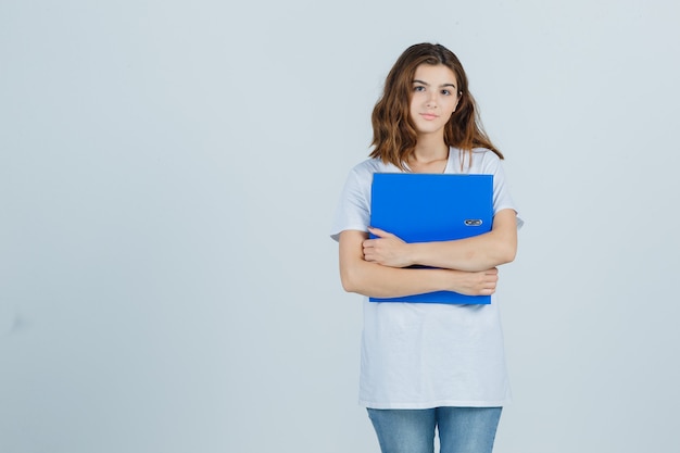 Young girl holding folder in white t-shirt and looking sensible , front view.