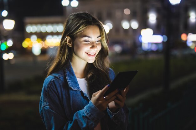 Young Girl holding in hands on blank screen tablet at night.