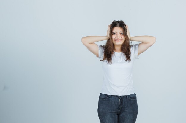 Young girl holding hands on head in t-shirt, jeans and looking confused , front view.