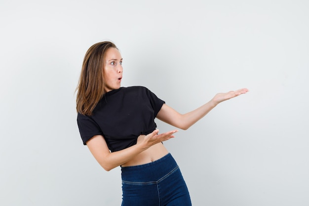 Free Photo young girl holding palms to show something terrible in black blouse, pants and looking scared