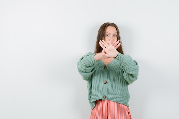 Young girl holding two hands crossed, gesturing x sign in knitwear, skirt and looking serious. front view.