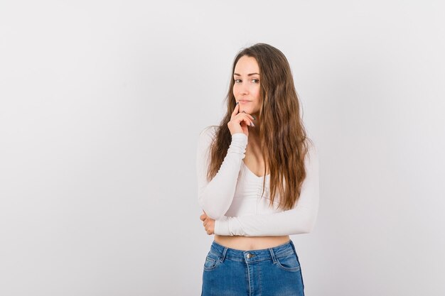 Young girl is looking at camera by holding forefinger on chin on white background