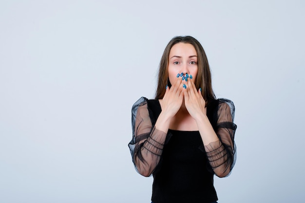 Free photo young girl is looking at camera by holding hands on mouth on white background