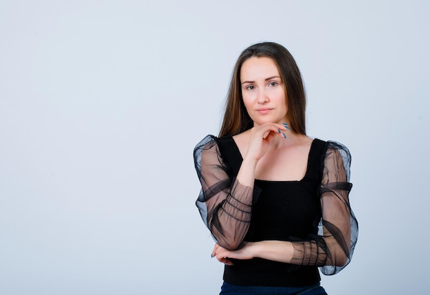 Young girl is looking at camera by putting hand under chin on white background