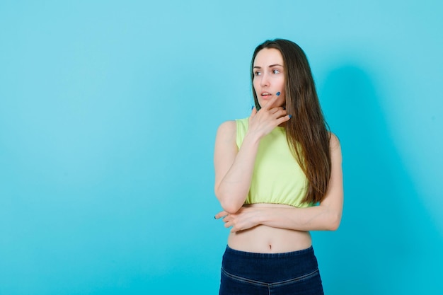 Young girl is looking at lest by putting hand on chin on blue background