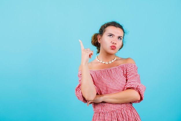 Young girl is looking and pointing up with forefinger on blue background