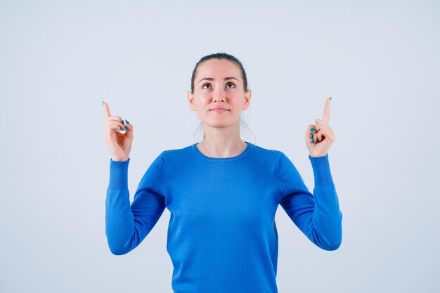 Young girl is looking up and pointing up with forefingers on white background