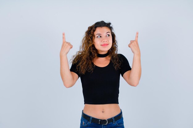 Young girl is looking up and pointing up with forefingers on white background