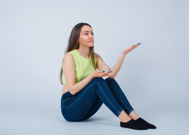 Young girl is pointing right up with hand by sitting on floor on white background