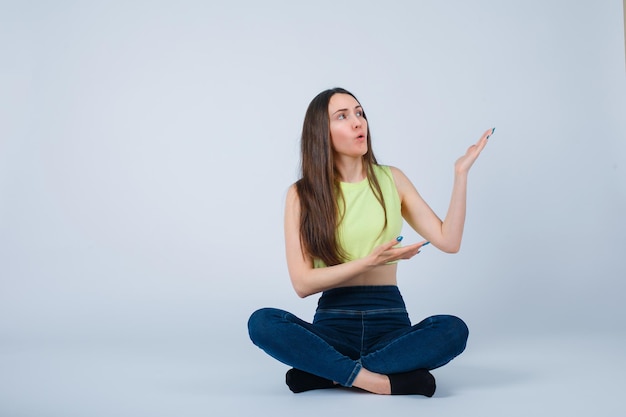 Young girl is pointing right with hands by sitting on floor on white background