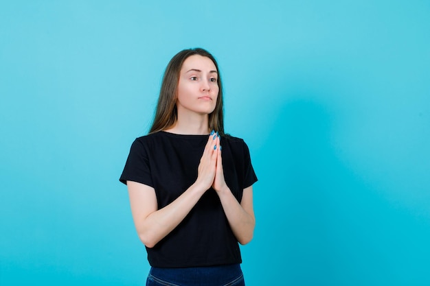 Young girl is praying by holding hands together on blue background