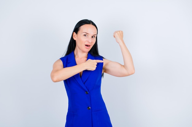 Young girl is raising up her muscle and showing it with forefinger on white background