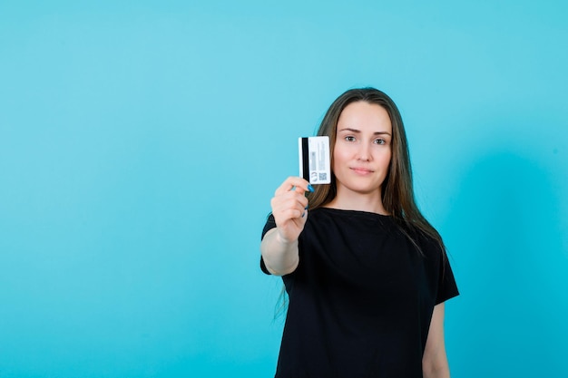 Young girl is showing credit card to camera on blue background